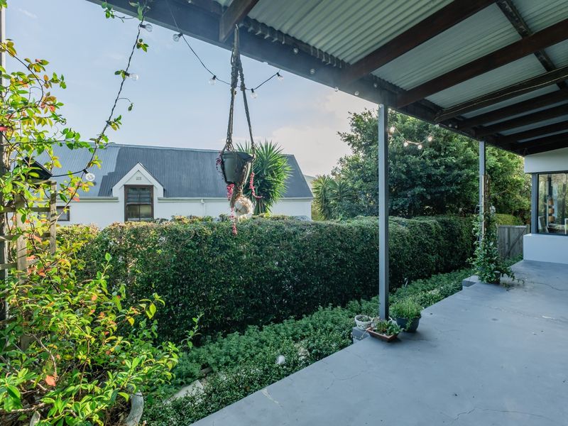 A covered outdoor patio area featuring a corrugated metal roof, steel support posts, and a painted concrete floor overlooking a landscaped garden.