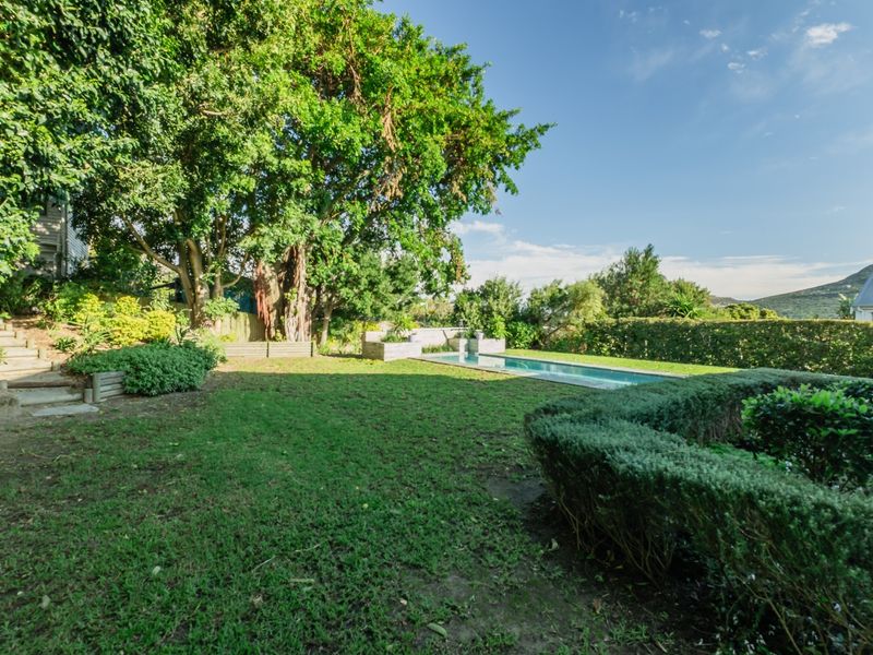 A spacious backyard featuring a rectangular swimming pool, mature trees, landscaped garden beds, and stone steps leading to an elevated area.