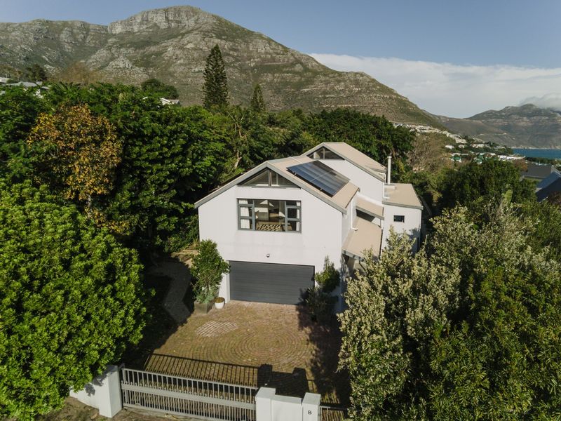 Aerial view of a modern residential property featuring a paved driveway, garage, and solar panels, set against a scenic mountain backdrop.