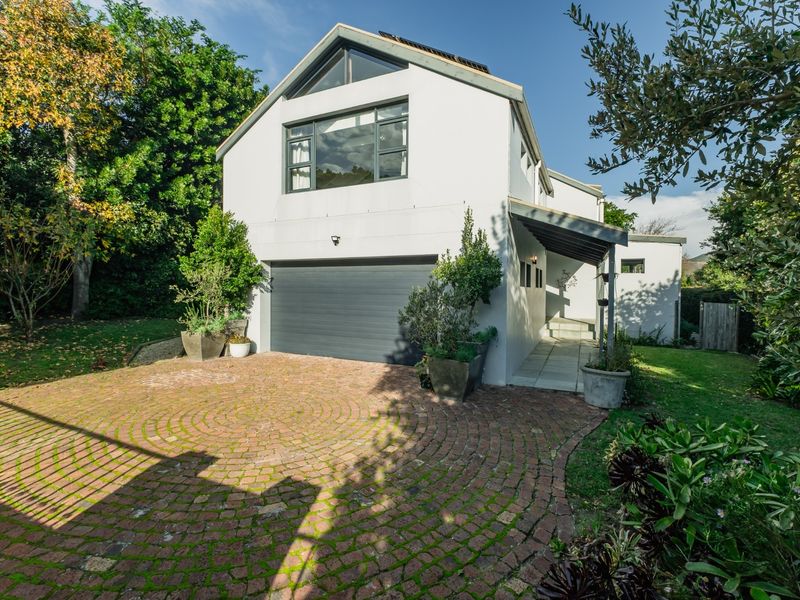 Front elevation of a modern home featuring a double garage, brick paved driveway, and a covered entrance walkway set within a landscaped garden.