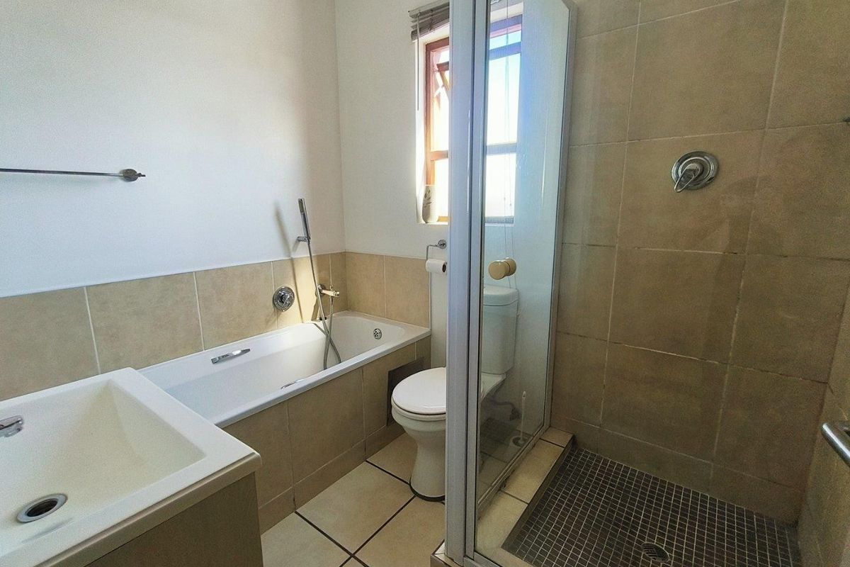 A functional bathroom featuring a built-in bathtub, separate glass-enclosed shower, toilet, and vanity basin with neutral wall and floor tiling.