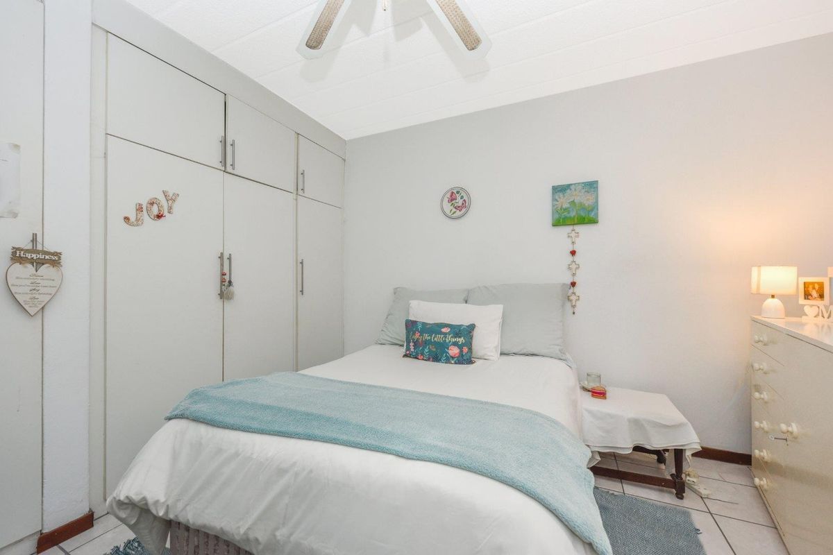 A functional bedroom featuring built-in cupboards, tiled flooring, and a ceiling fan.