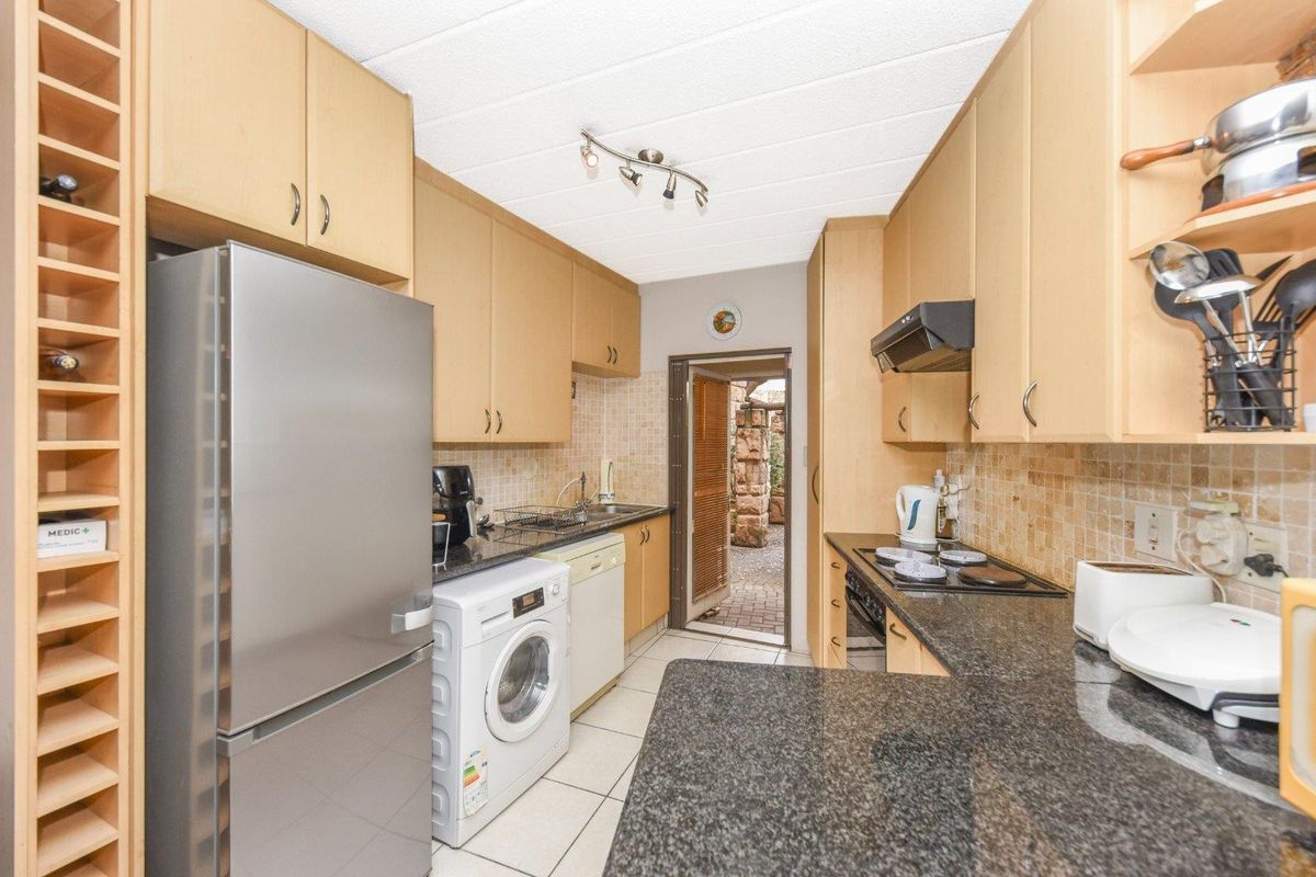 A functional galley-style kitchen featuring light wood cabinetry, granite countertops, tiled backsplash, and integrated stove and extractor fan.