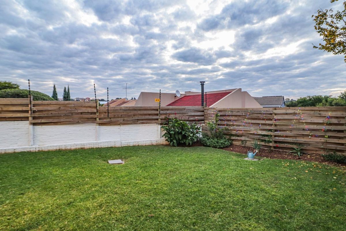 A private rear garden featuring a well-maintained lawn, enclosed by timber slat fencing and a painted brick boundary wall.