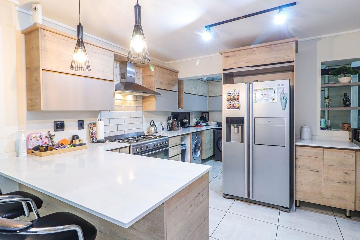 Modern kitchen featuring light wood cabinetry, white stone countertops, a gas stove with extractor fan, and integrated laundry appliances.