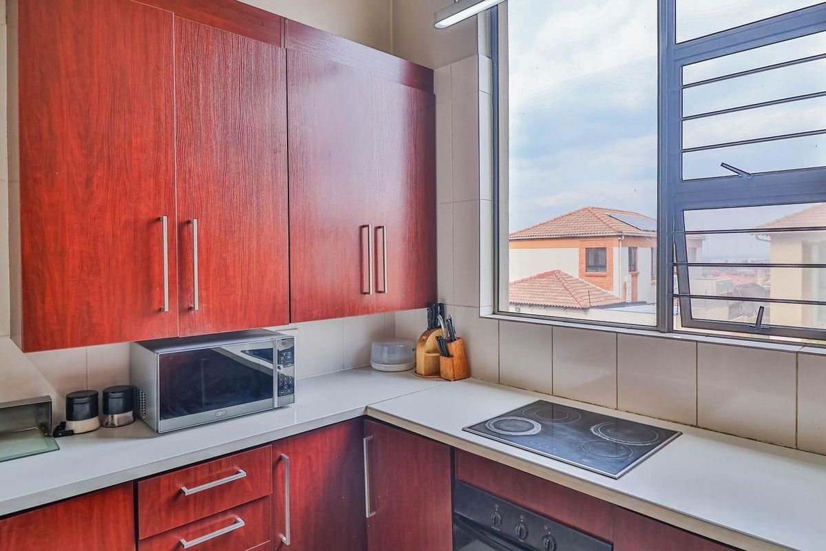 A functional kitchen featuring dark wood-toned cabinetry, a built-in electric hob, an under-counter oven, and a large window providing natural light.