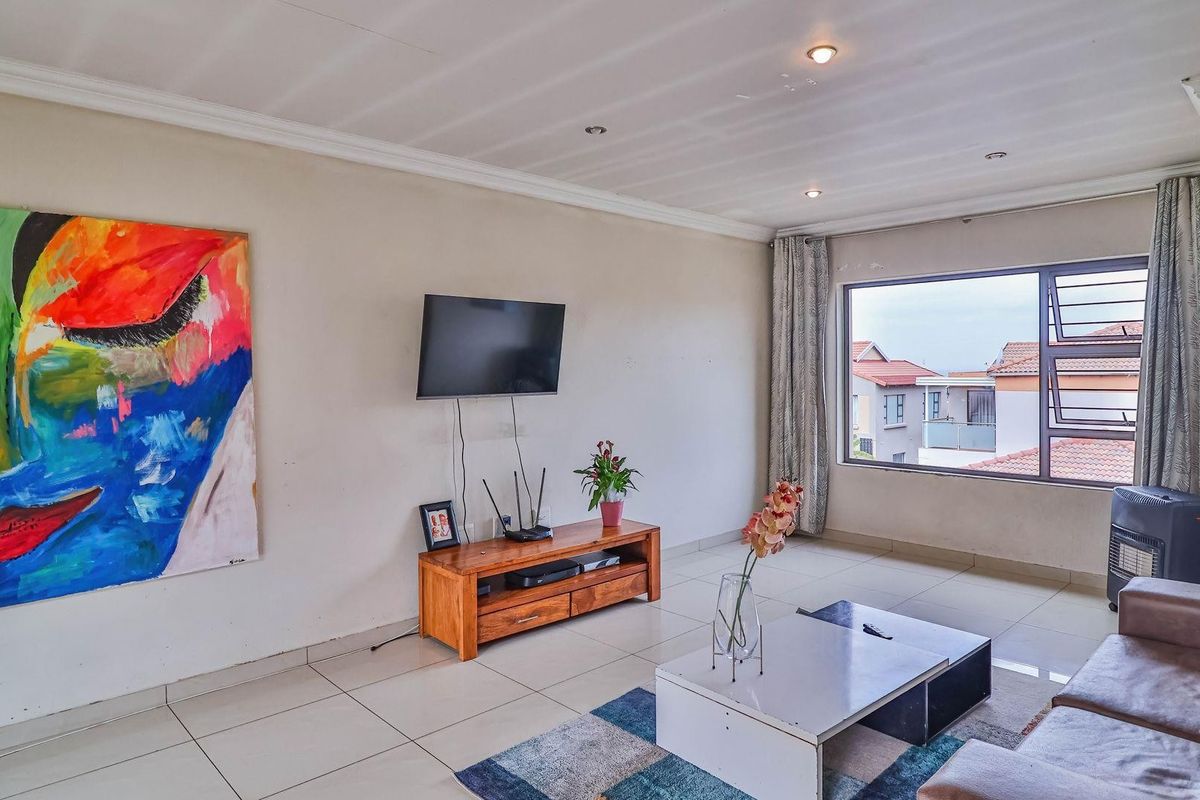A bright living room featuring large windows, tiled flooring, and recessed ceiling lighting, offering a comfortable and functional space.