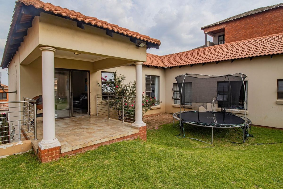 A rear view of the house featuring a covered patio with tiled flooring, columns, and a small adjacent garden area.