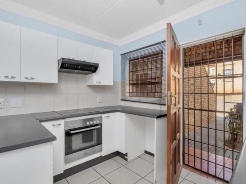 Functional kitchen featuring white cabinetry, dark countertops, built-in oven, extractor fan, and direct access to an exterior courtyard through a security gate.