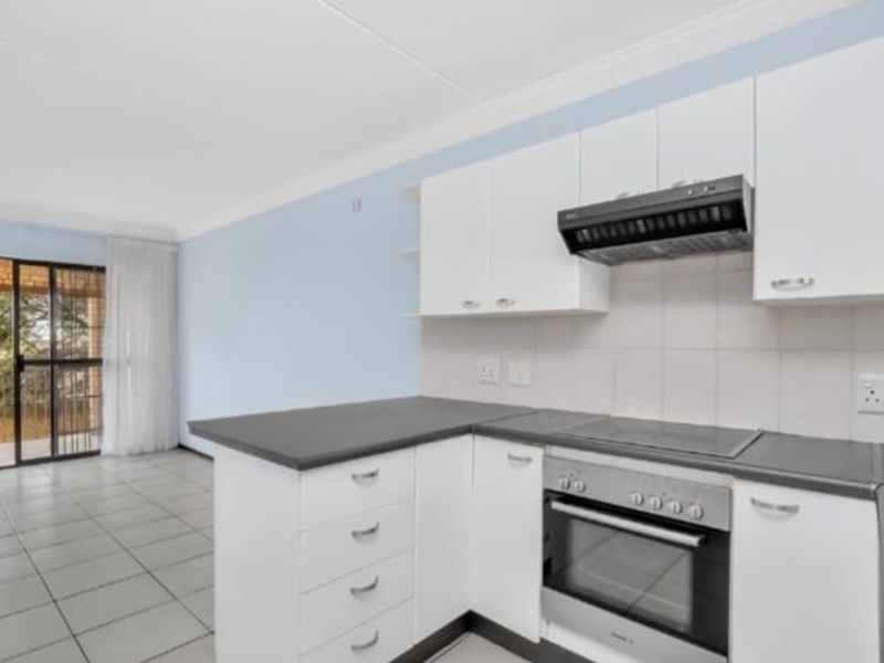 A bright open-plan kitchen featuring white cabinetry, dark countertops, a built-in oven, and an extractor fan, with direct access to an outdoor balcony area.