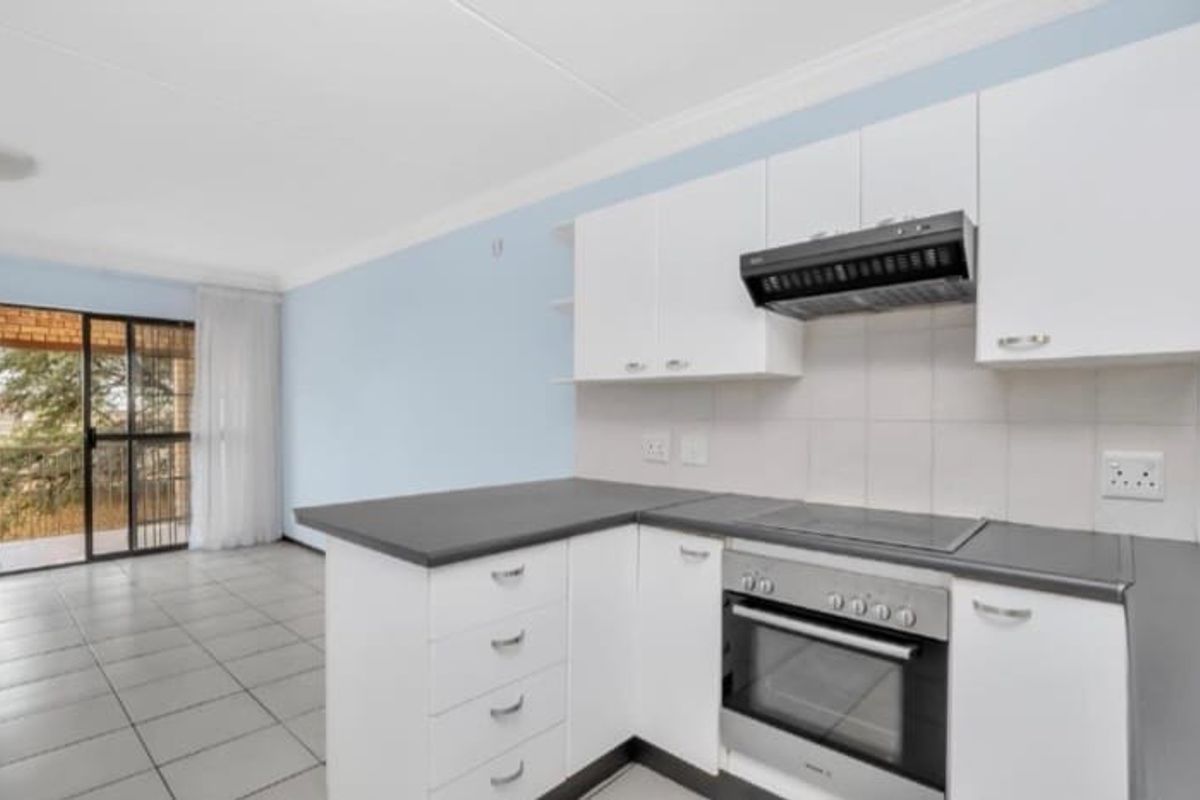 A bright open-plan kitchen featuring white cabinetry, dark countertops, a built-in oven, and an extractor fan, with direct access to an outdoor balcony area.
