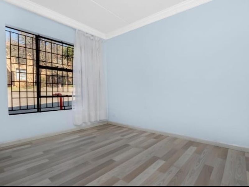 A bright, empty bedroom featuring light-toned wood-look flooring, crown molding, and a large window fitted with security bars.
