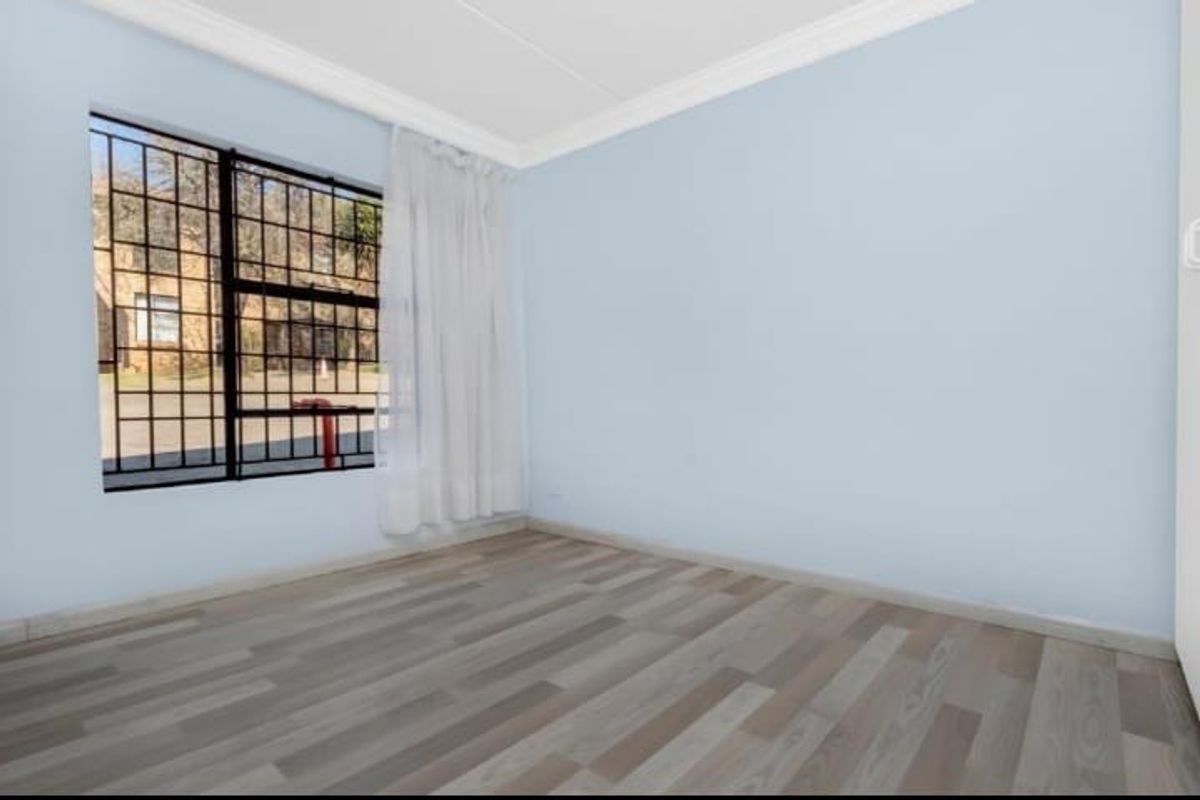 A bright, empty bedroom featuring light-toned wood-look flooring, crown molding, and a large window fitted with security bars.