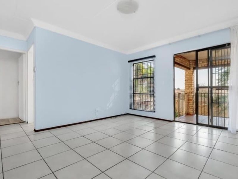 A bright, empty living room featuring tiled flooring, large windows with security bars, and sliding glass doors leading to an outdoor patio area.