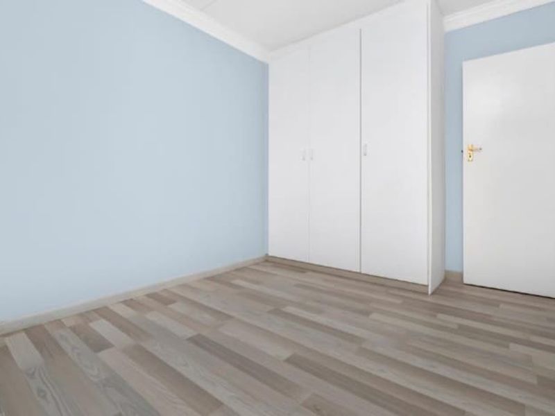 A bright, empty bedroom featuring light-toned wood-look flooring, built-in white cabinetry, and soft blue wall paint.
