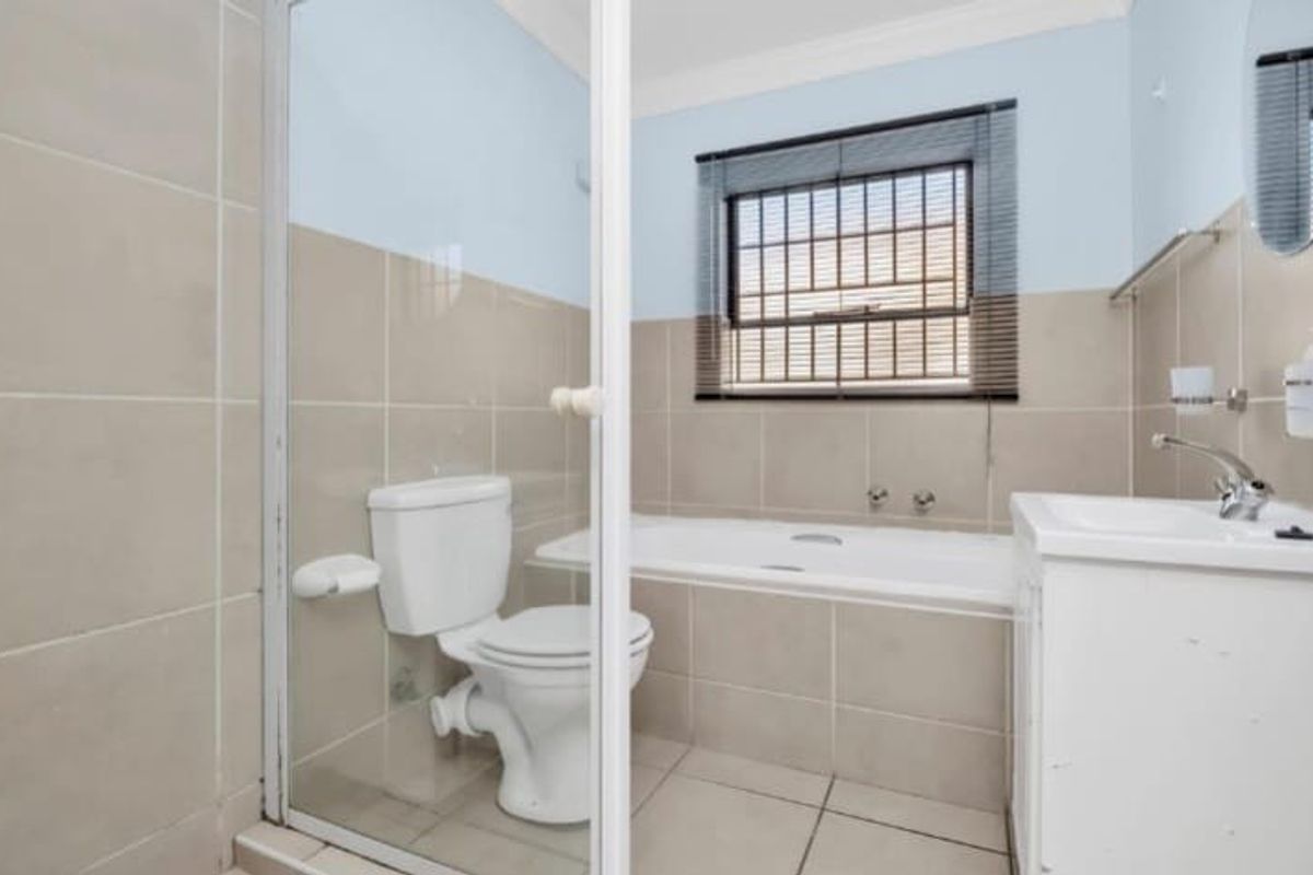 A functional bathroom featuring a built-in bathtub, a separate shower enclosure, and a vanity basin with tiled walls and flooring.