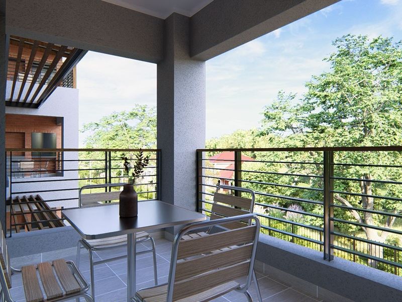 A modern covered balcony featuring tiled flooring and a sleek metal railing, offering pleasant views of the surrounding greenery.