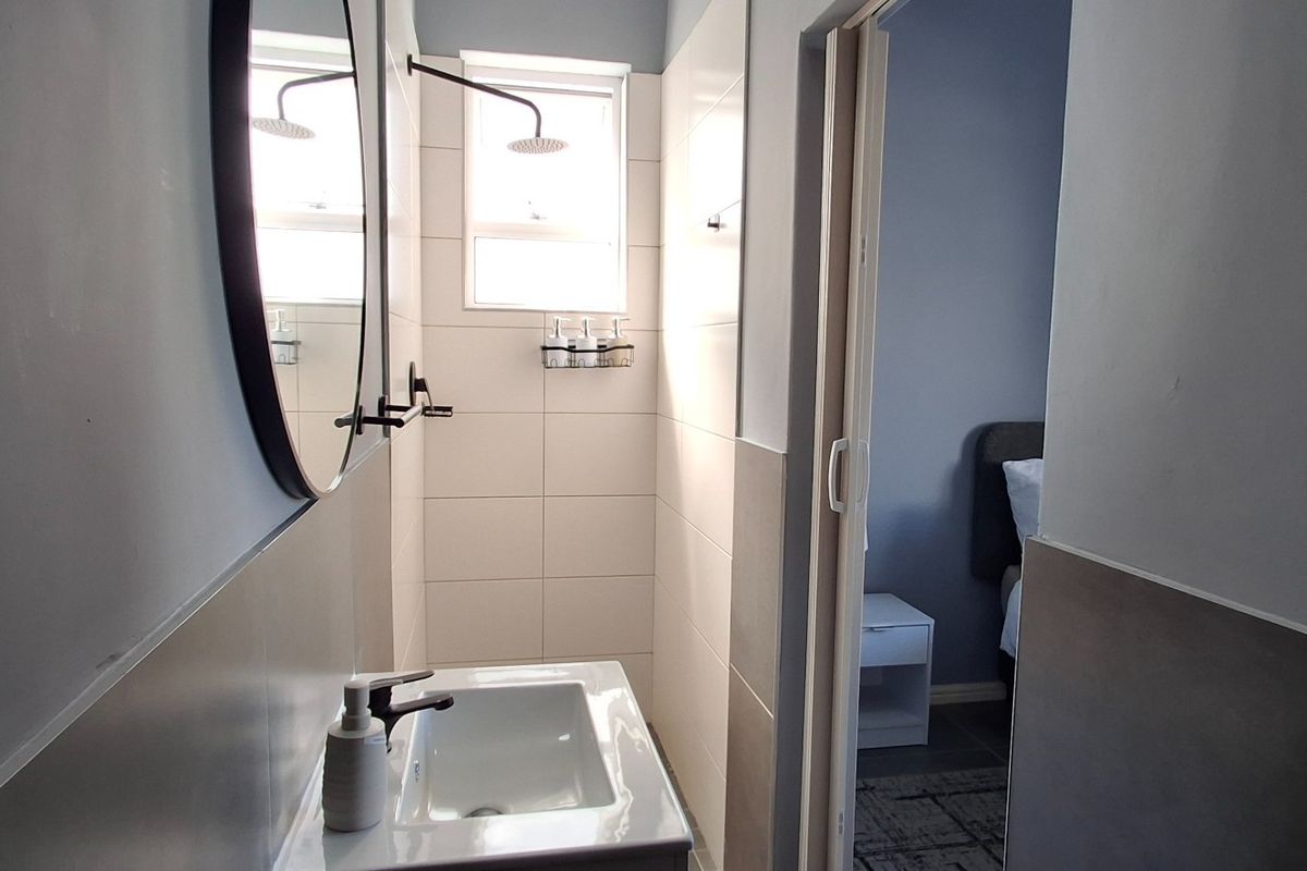 A modern bathroom featuring a wall-mounted basin, a walk-in shower with a rainfall showerhead, and neutral wall tiling.
