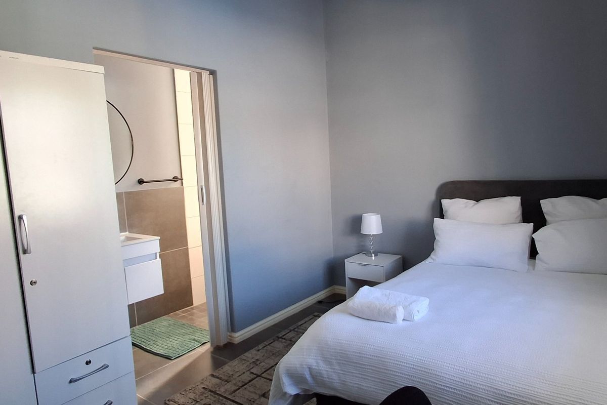 A well-maintained bedroom featuring neutral wall tones, an en-suite bathroom with modern tiling, and a clean, functional layout.