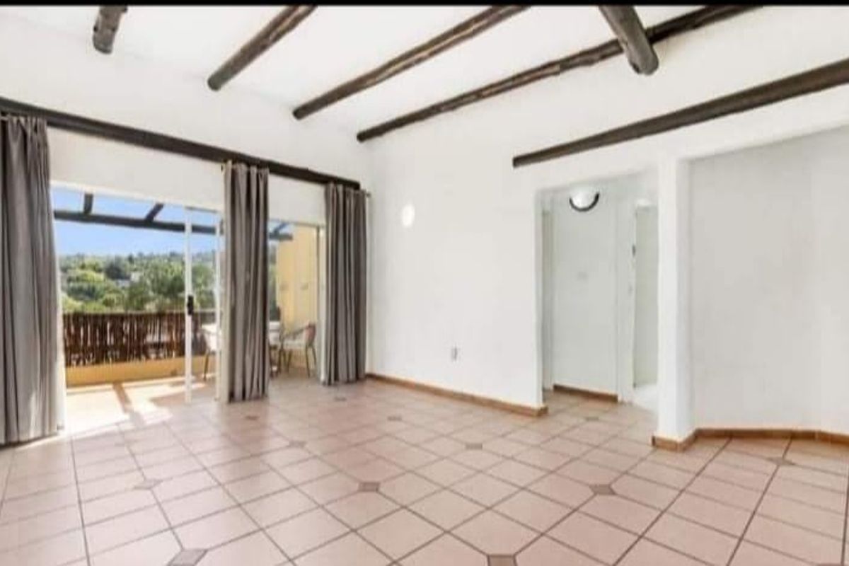 Spacious living area featuring exposed timber ceiling beams, tiled flooring, and large sliding glass doors opening onto a private balcony.