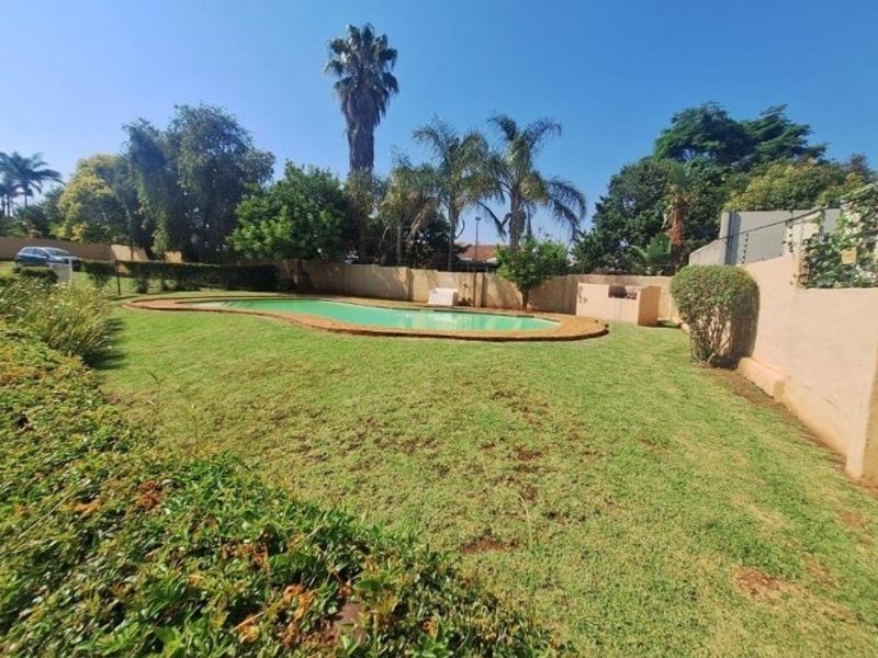 Spacious backyard featuring a swimming pool, built-in braai area, and established lawn enclosed by perimeter walls.