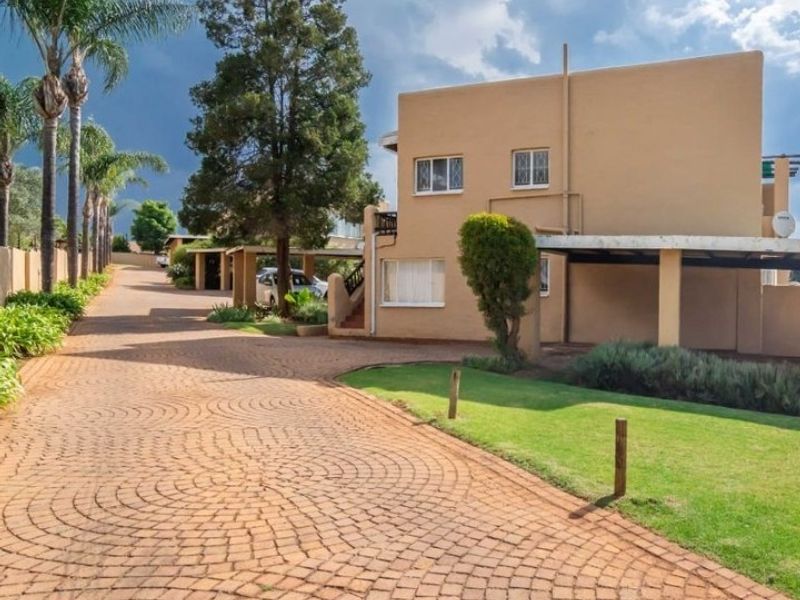 A view of the townhouse exterior featuring a paved driveway, covered carport, and well-maintained garden area.