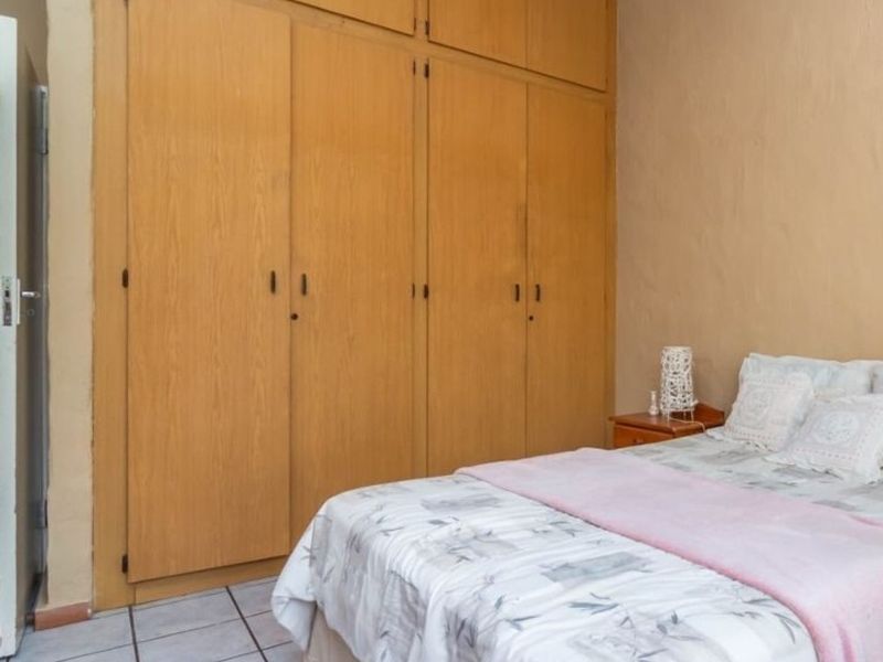 A bedroom featuring floor-to-ceiling built-in wooden cupboards and tiled flooring.