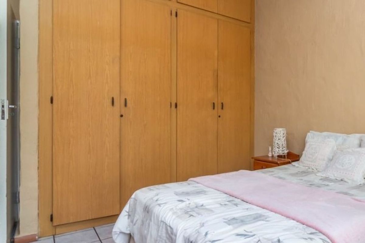 A bedroom featuring floor-to-ceiling built-in wooden cupboards and tiled flooring.