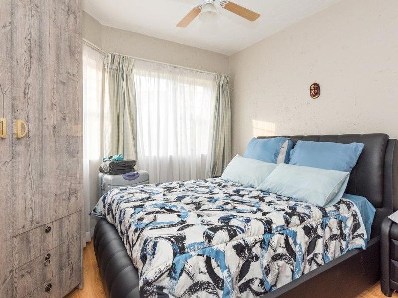 A cozy bedroom featuring a built-in wardrobe, ceiling fan, and laminate flooring, offering a functional and comfortable living space.