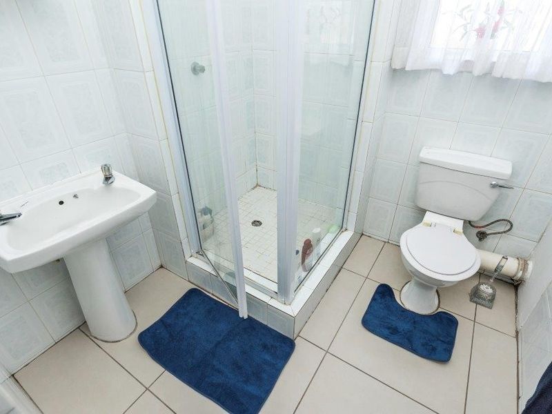 A functional bathroom featuring a pedestal basin, a shower enclosure, and a toilet, with tiled finishes throughout.