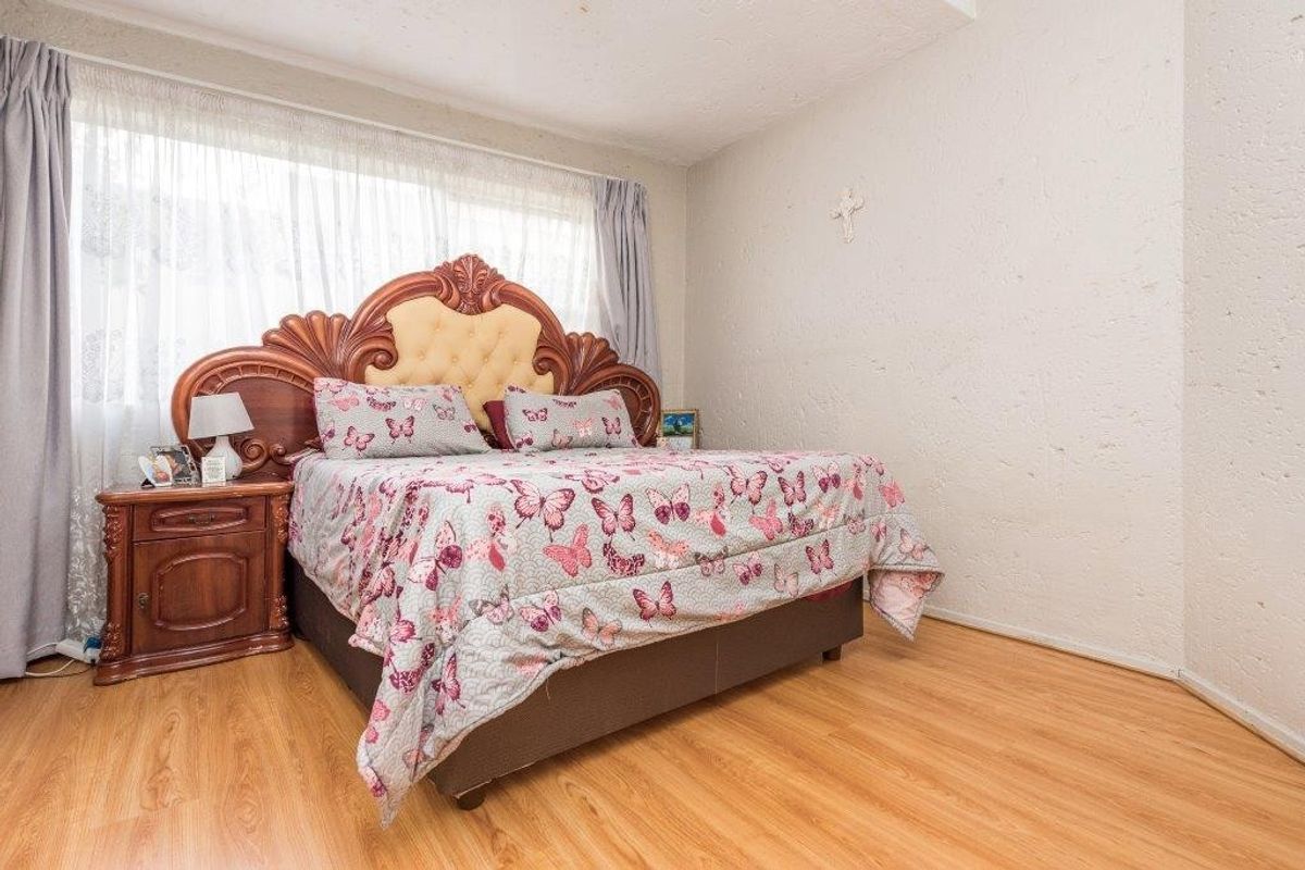 A bedroom featuring laminate flooring and large windows with curtain rails, providing a functional and well-lit space.