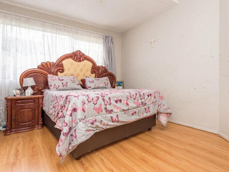A bedroom featuring laminate flooring and large windows with curtain rails, providing a functional and well-lit space.