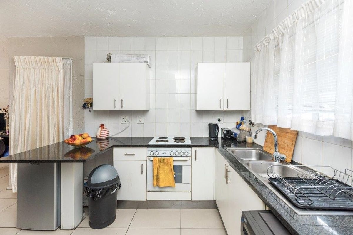 Functional kitchen featuring white cabinetry, granite countertops, electric hob, oven, and double basin sink with tiled splashbacks and flooring.