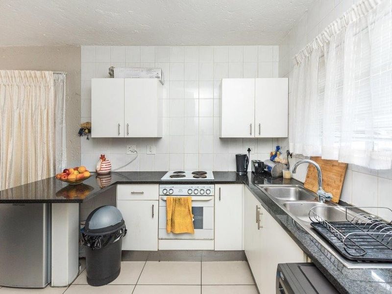 Functional kitchen featuring white cabinetry, granite countertops, electric hob, oven, and double basin sink with tiled splashbacks and flooring.