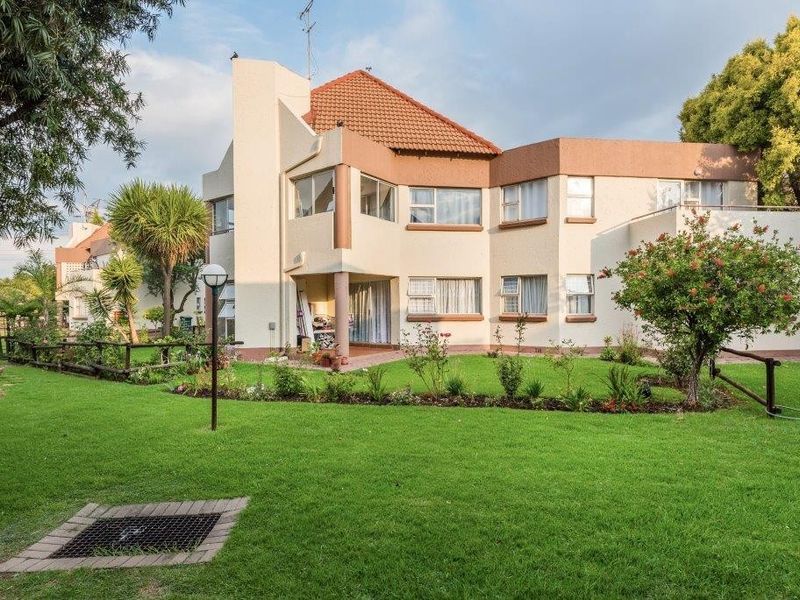 Rear view of the townhouse featuring a well-maintained garden, covered patio area, and traditional tiled roof architecture.