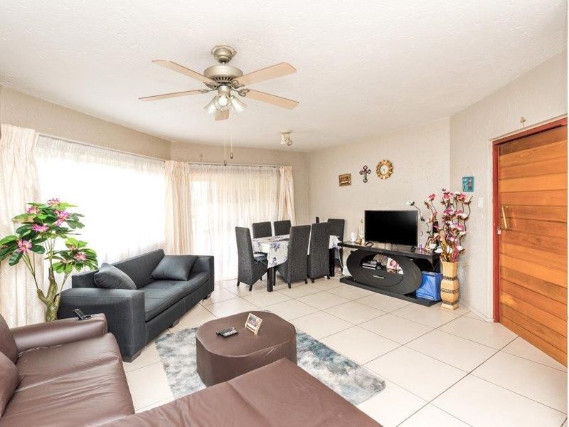 Spacious open-plan living and dining area featuring neutral tiled flooring, a ceiling fan, and direct access to the exterior via a sliding glass door.