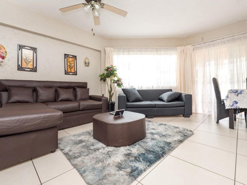 Spacious open-plan living and dining area featuring neutral tiled flooring, a ceiling fan, and large windows providing ample natural light.