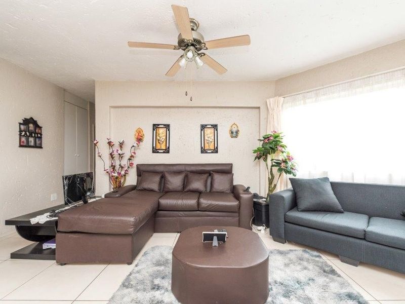 A spacious living room featuring tiled flooring, a ceiling fan, and a large window allowing for natural light.