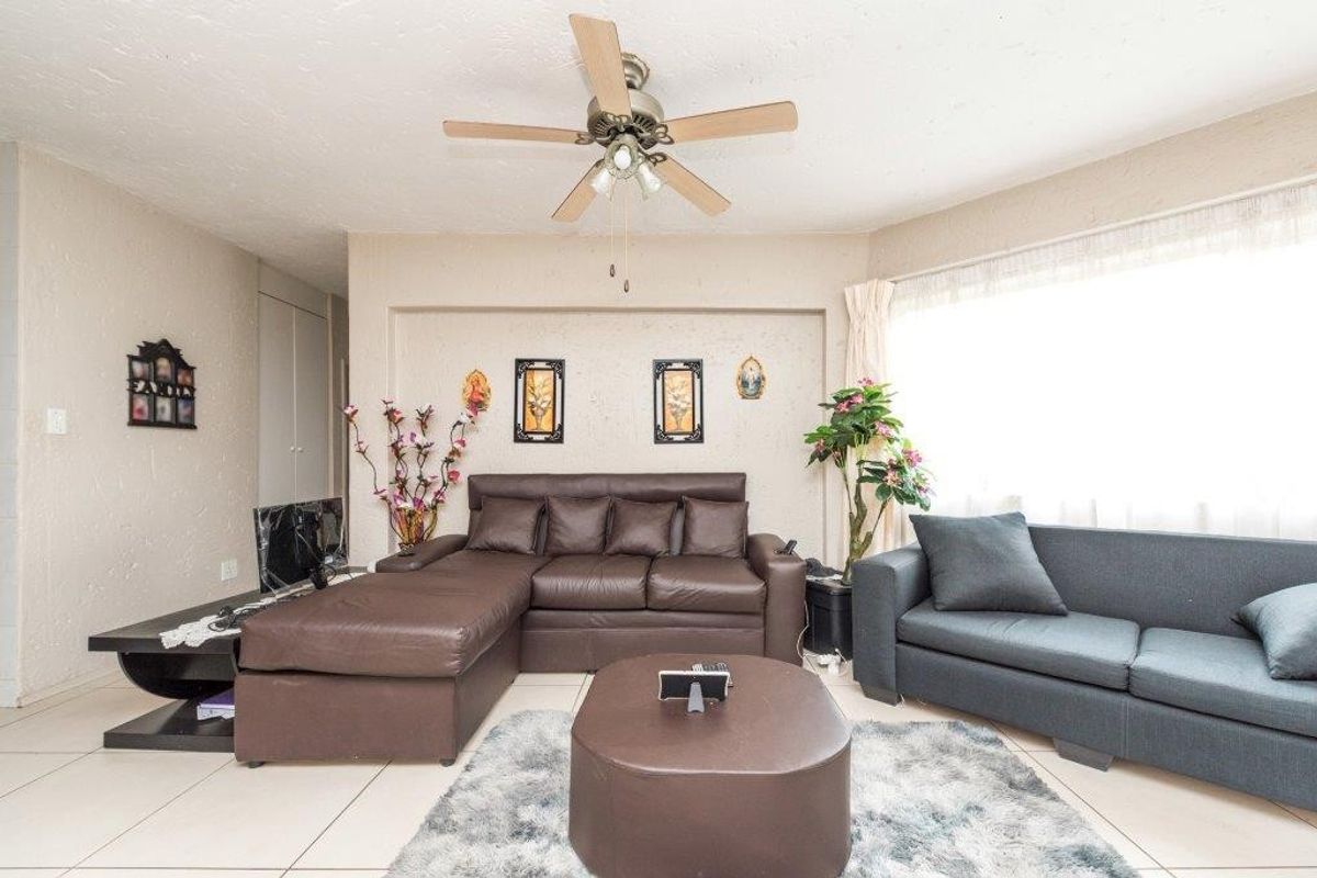 A spacious living room featuring tiled flooring, a ceiling fan, and a large window allowing for natural light.