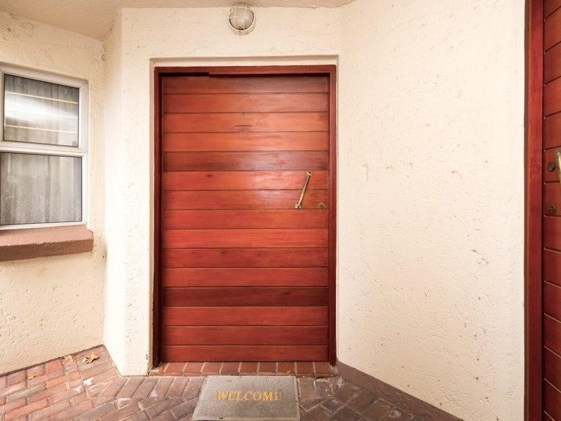 A private townhouse entrance featuring a solid timber front door, brick paved threshold, and exterior bulkhead lighting.
