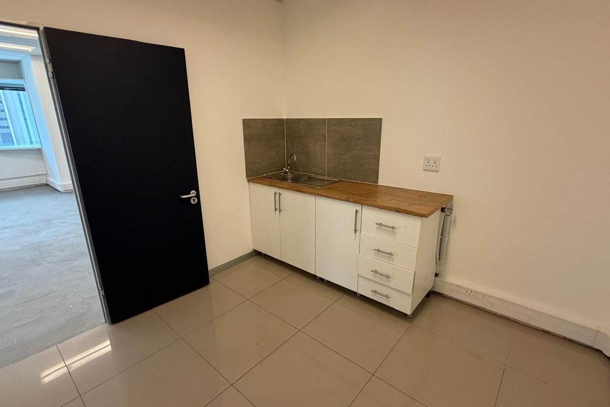 A compact office kitchenette featuring white cabinetry, a wooden countertop, a stainless steel sink, and tiled flooring.