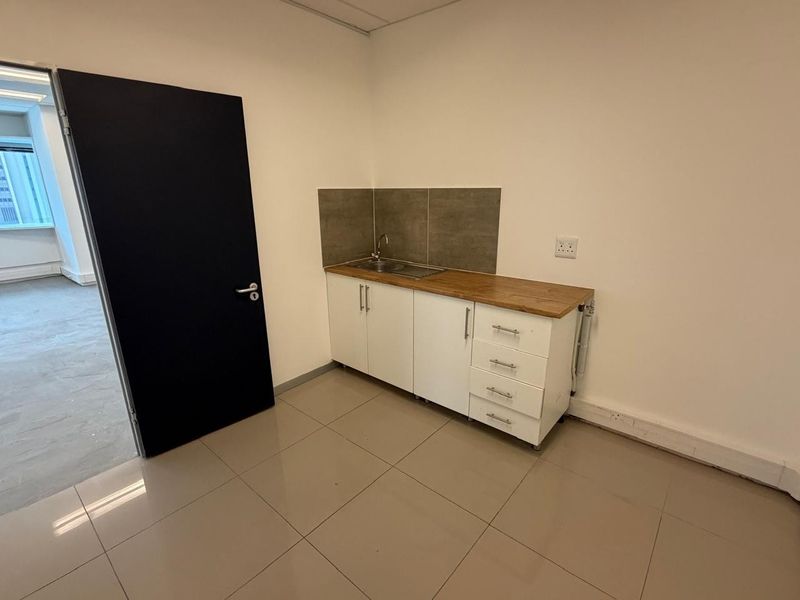 A compact office kitchenette featuring white cabinetry, a wooden countertop, a stainless steel sink, and tiled flooring.