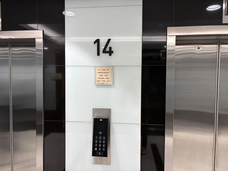 Modern office building elevator lobby on the 14th floor featuring stainless steel lift doors and a digital access control keypad.