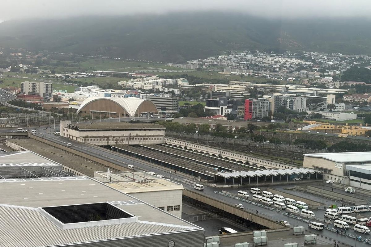 Elevated aerial view overlooking a city transport hub, railway lines, and surrounding urban infrastructure under a cloudy sky.