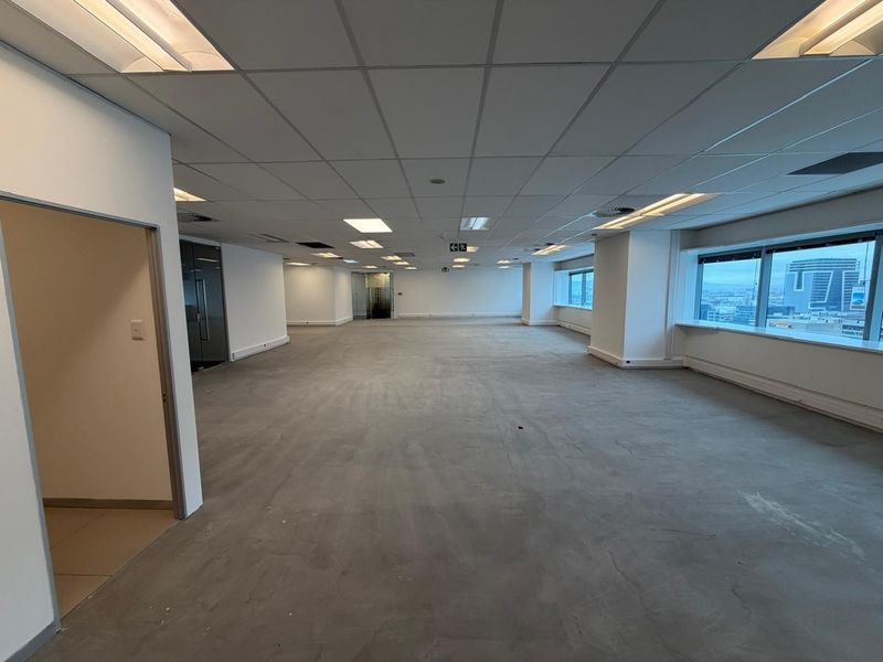 Spacious open-plan office area featuring a suspended ceiling, large windows with city views, and unfinished concrete flooring ready for custom finishes.