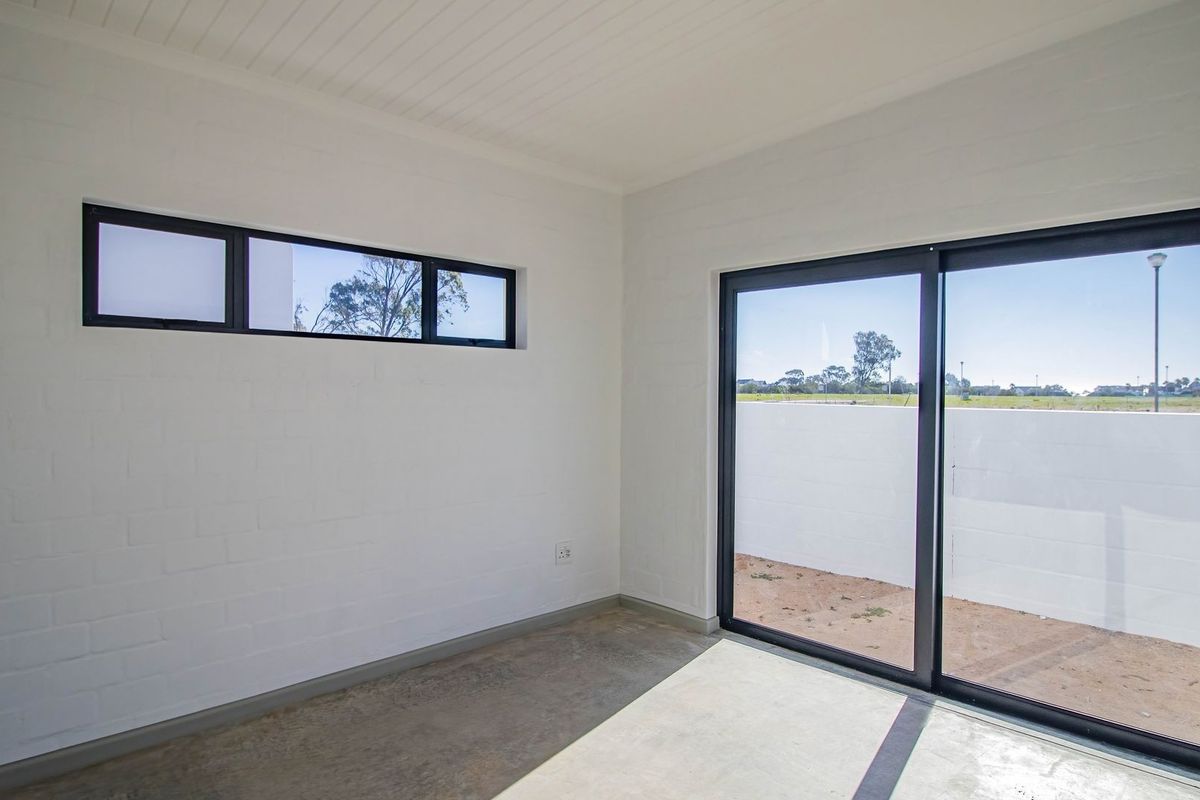A bright, empty room featuring white painted brick walls, polished concrete flooring, and large black-framed sliding glass doors leading to an outdoor area.