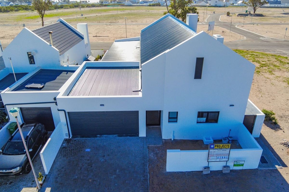 Aerial view of a modern white house featuring a dark metal roof, paved driveway, and attached garage in a developing residential estate.
