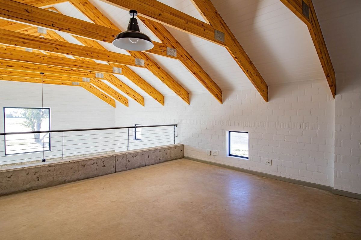 Spacious loft-style living area featuring exposed timber roof trusses, polished concrete flooring, and a modern metal balustrade overlooking the lower level.