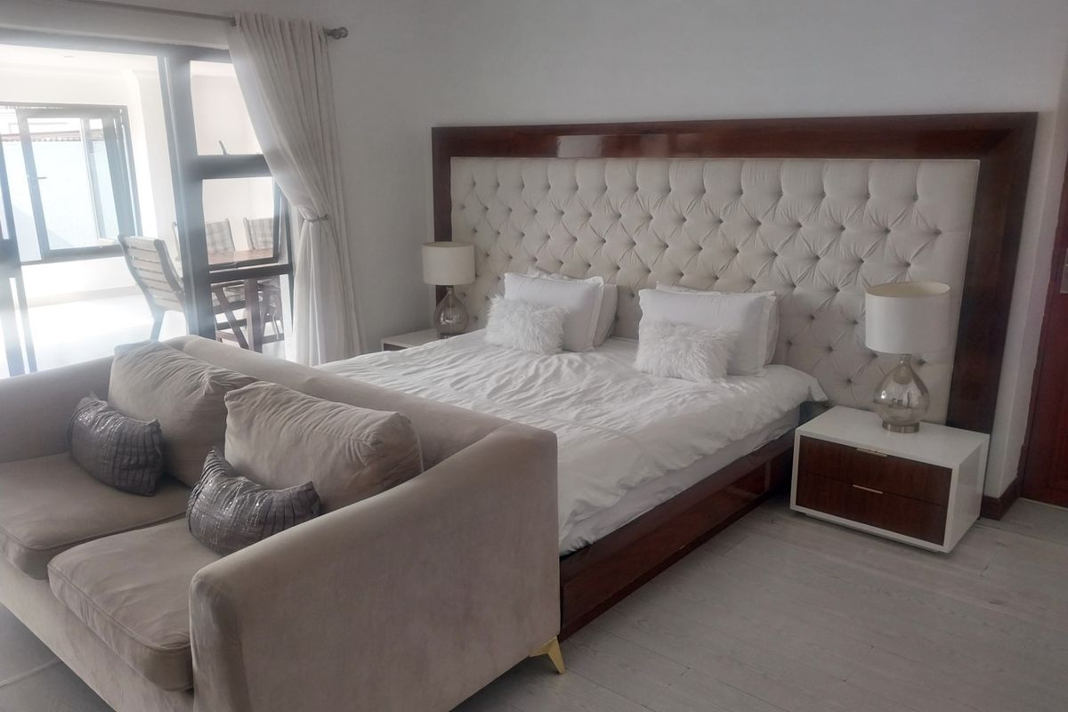 Spacious bedroom featuring a large tufted headboard, light wood-look flooring, and direct access to an outdoor patio area through sliding glass doors.