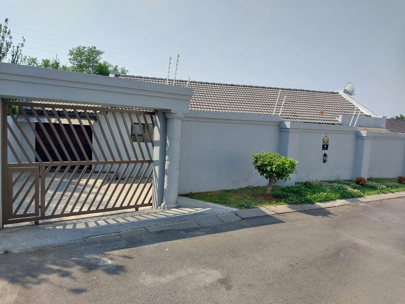Front view of the property featuring a secure perimeter wall, tiled roof, and a metal sliding gate providing access to the driveway.